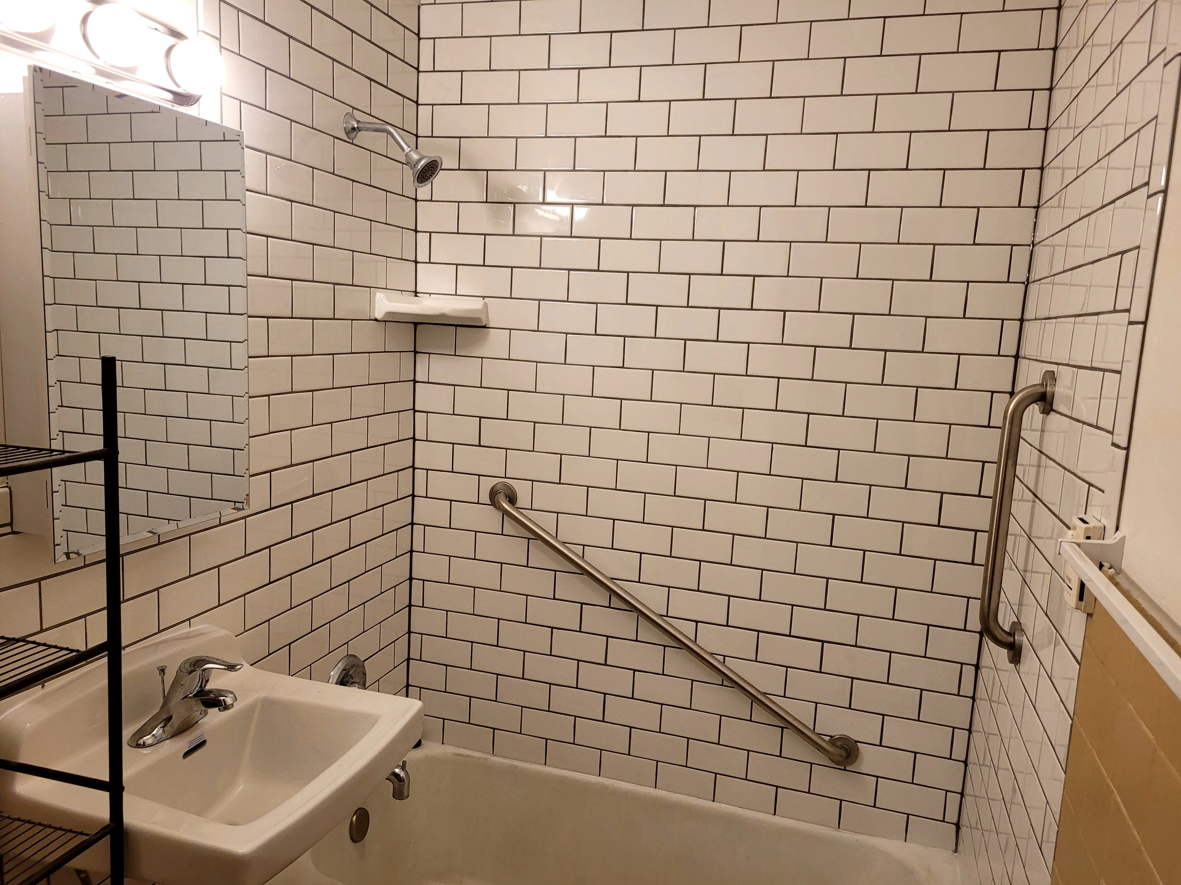 After — Small bathroom remodel. Before: dingy old yellow 4x4 tile, dated wood vanity, scratched cast-iron tub. After: white subway tile with dark grout, hex floor tile, new sink and tub. Yellow tile remnants still visible behind new subway tile in after shot confirms same room.