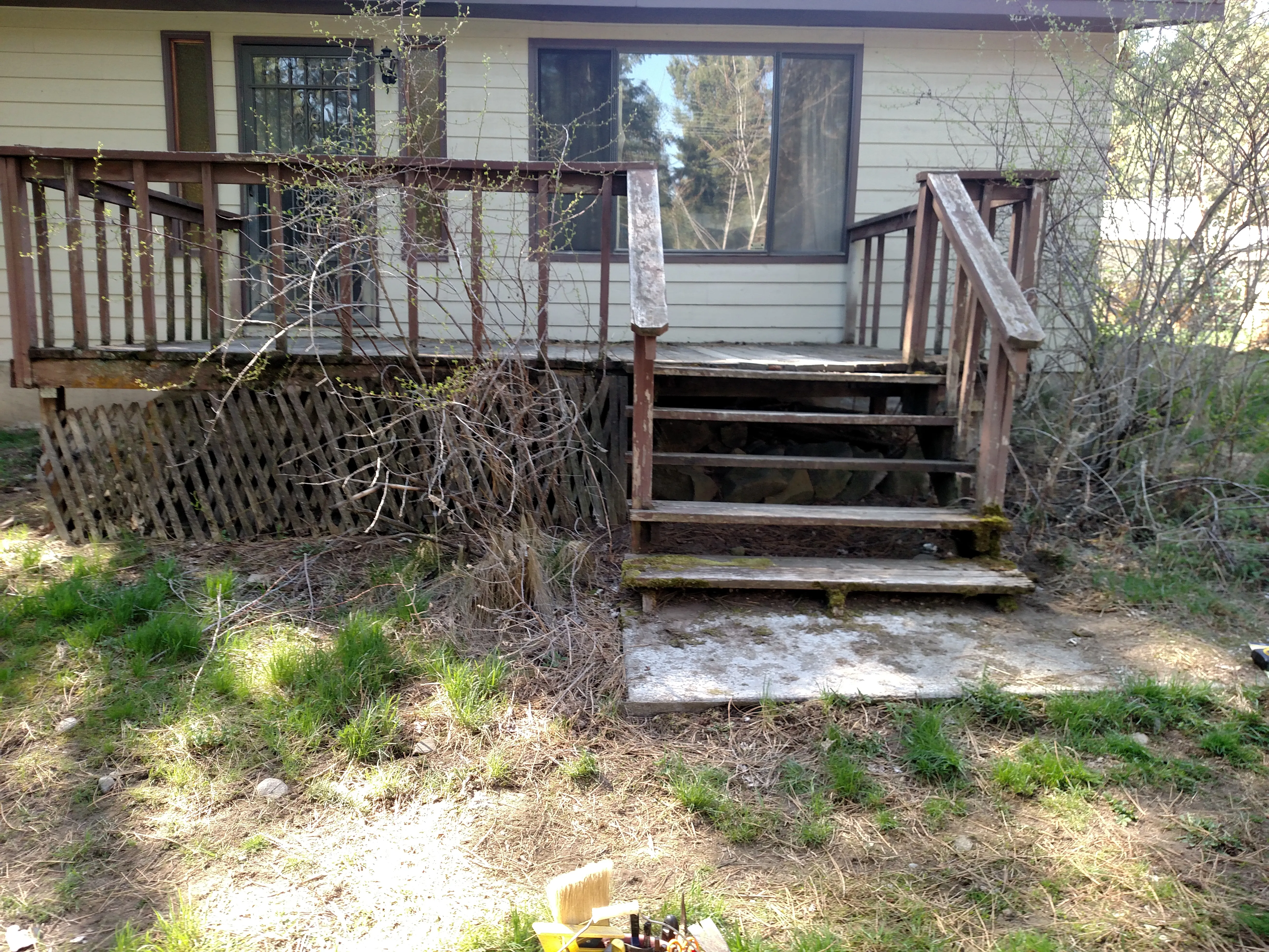 Before — Backyard deck rebuild. Before: rotting wood deck with broken lattice skirt and weathered steps. After: new composite deck boards with black metal balusters and stairs leading to backyard.